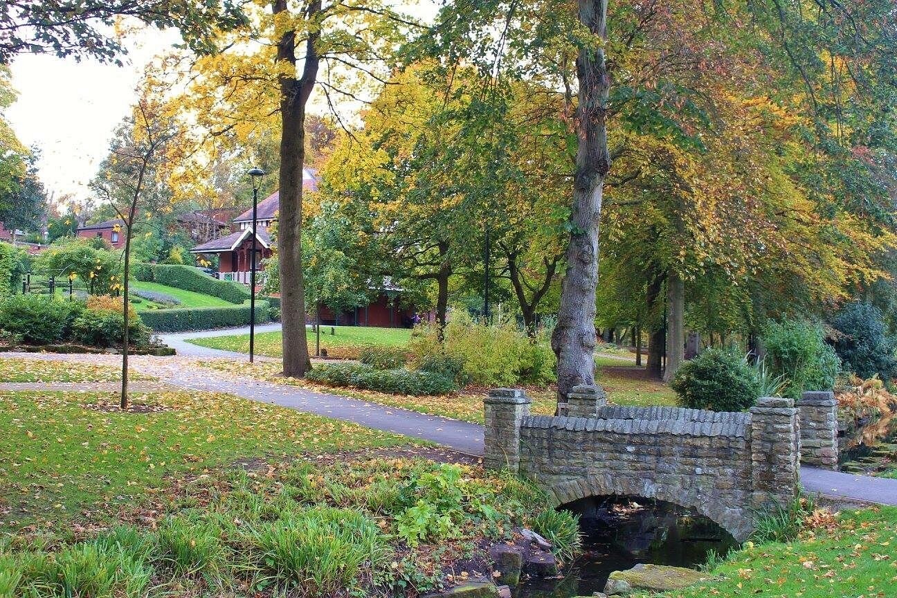 Stone bridge over a stream in Walsall Arboretum with autumn trees